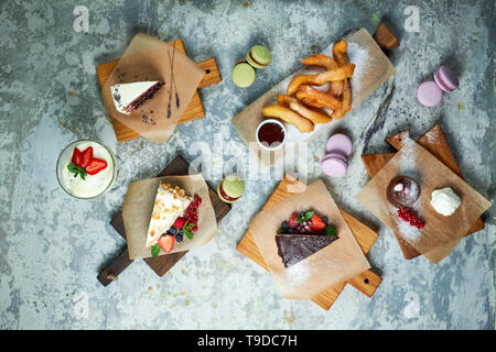 Un assortimento di dolci: torta, churos, rotolo di meringa, gelato, decorata con frutti di bosco su tavole di legno. Vista dall'alto. Grigio sfondo a trama. Bellissimi piatti di servizio. Il dessert. La catena alimentare Foto Stock