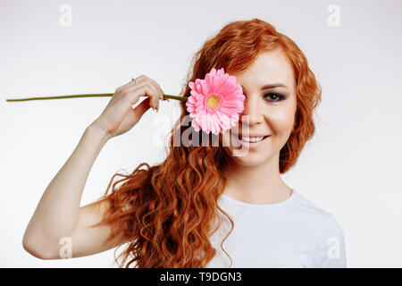 Bellezza nella primavera del concetto. Adorabili, bella carino sorridendo felice donna in abiti casual con sorriso tenendo una gerbera su di un occhio. Ritratto di bellezza ho Foto Stock