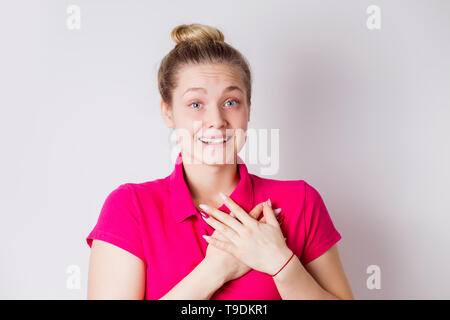 Gioiosa felice giovane donna sorride eccitato, è sorpreso e tiene le mani sul cuore su sfondo bianco. Emozioni positive, l'espressione del viso, gesti c Foto Stock