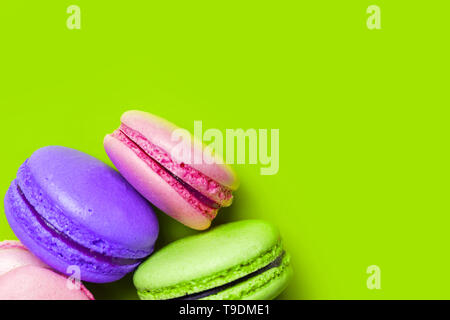 Primo piano della coloratissima amaretti dolce su uno sfondo verde con copia spazio, vista dall'alto. Francese per dessert serviti con il tè del pomeriggio o caffè Foto Stock