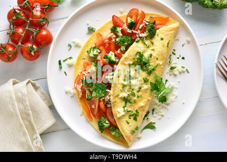 Riempite la frittata con pomodori, peperone rosso e i broccoli sulla luce sullo sfondo di legno. Alimentazione sana alimenti per la colazione. Gustoso cibo di mattina. Vista dall'alto, Foto Stock