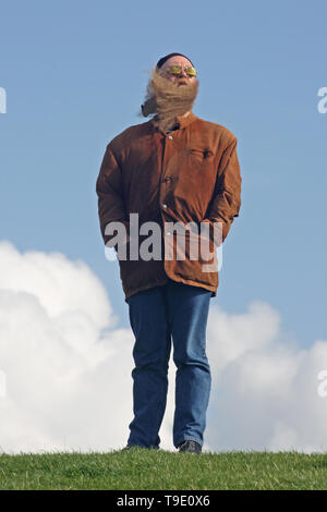 Mann mit langem Bart, der vom Wind verwirbelt wurde, steht am Ufer des Meeres Foto Stock