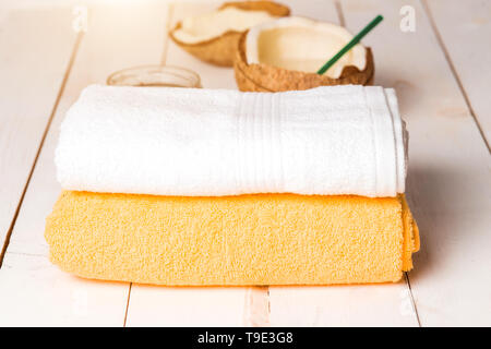 Spa con due giallo pulito e gli asciugamani bianchi, scrub organico in un barattolo di vetro, olio di noce di cocco per massaggio su un tavolo di legno. Latte di cocco, acqua, cocktail. Ri Foto Stock