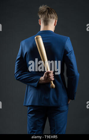 Aggressività latente. Imprenditore o un uomo in abito formale nasconde mazza di legno dietro la schiena, sfondo scuro. Pericolo nascosto concetto. Uomo con bat nasconde il suo aggr Foto Stock