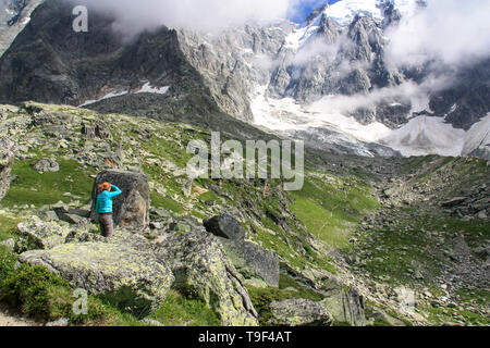 Redhead donna in piedi tra massi e rocce ad esplorare il massiccio del Monte Bianco e guardando verso il picco dell'Aiguille du Midi in Francia Foto Stock