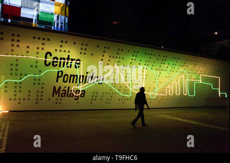 Malaga, Spagna. 19 Maggio, 2019. Un uomo cammina passato attraverso la facciata del Centro Pompidou Museo decorata con una illuminazione artistica durante 'la notte in bianco" 2019. Ogni maggio, Malaga celebra una notte culturale con più di 200 attività nel centro della città come prestazioni, Arte di strada, musica dal vivo e visite gratuite in tutti i musei. Credito: SOPA Immagini limitata/Alamy Live News Foto Stock