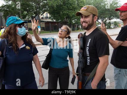 Un sostenitore di Ilhan Omar (centro) affronta anti-Musulmano manifestanti, alcune aperture che trasportano armi legalmente, al di fuori di una Austin, Texas, l'hotel dove il controverso congressista musulmano ha parlato a una città-wide iftar cena. Foto Stock