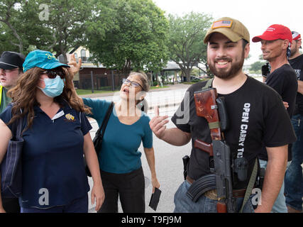 Un sostenitore di Ilhan Omar (centro) affronta anti-Musulmano manifestanti, alcune aperture che trasportano armi legalmente, al di fuori di una Austin, Texas, l'hotel dove il controverso congressista musulmano ha parlato a una città-wide iftar cena. Foto Stock