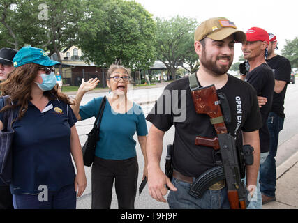 Un sostenitore di Ilhan Omar (centro) affronta anti-Musulmano manifestanti, alcune aperture che trasportano armi legalmente, al di fuori di una Austin, Texas, l'hotel dove il controverso congressista musulmano ha parlato a una città-wide iftar cena. Foto Stock