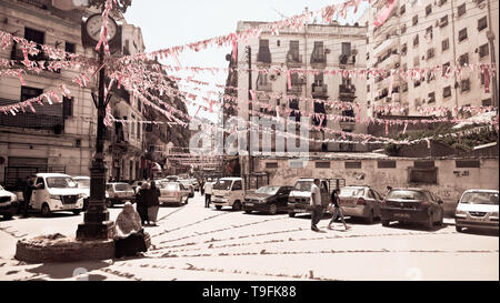 Vecchia donna seduta accanto alla colonna di clock a una piazza decorata in un quartiere residenziale di Algeri, Algeria, durante il Ramadan Foto Stock