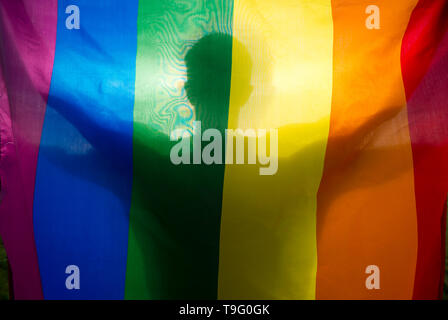 Close-up silhouette ombra di un uomo in possesso di un gay pride bandiera arcobaleno con le braccia aperte retroilluminati da golden sun Foto Stock
