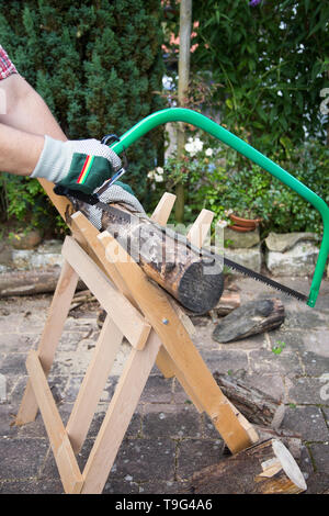 Segatura di legna da ardere manualmente con un seghetto a mano su una tavola di legno sawhorse Foto Stock