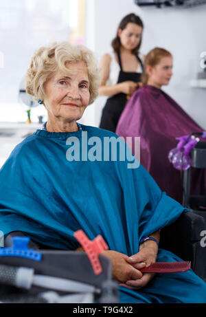 Eleganti Donna senior per parrucchieri capo seduto nella sedia del barbiere, attesa per il taglio dei capelli Foto Stock