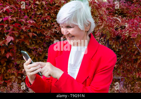 Ritratto di vecchia signora, nonna selfie rende all'aperto presso sun giorno. moderno granny caucasica dito toccare il touchscreen del suo telefono. Ella ha smartphone Foto Stock