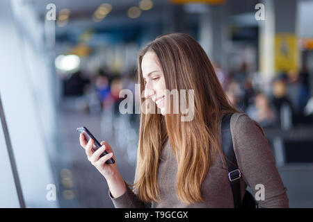 Giovane imprenditrice utilizza lo smartphone all'aeroporto. Donna sorridente con un telefono cellulare per un viaggio di lavoro Foto Stock