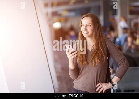 Giovane donna utilizza lo smartphone all'aeroporto. Ragazza sorridente con un telefono cellulare sul viaggio di vacanza Foto Stock