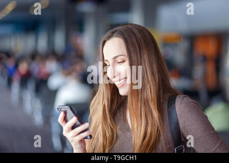 Giovane donna utilizza lo smartphone all'aeroporto. Ragazza sorridente con un telefono cellulare sul viaggio di vacanza Foto Stock