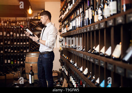 L'uomo la lettura del contenuto di una bottiglia di vino. close up vista laterale foto. il gusto della preferenza. vino elegante Foto Stock