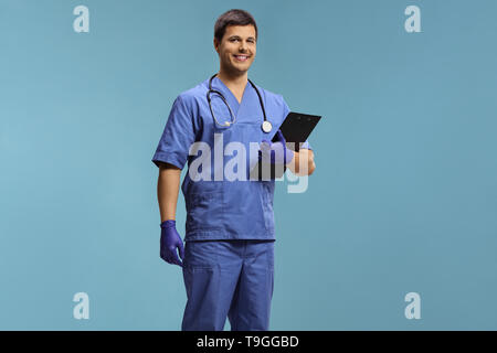 Giovane maschio medico in un'uniforme che indossano guanti e tenendo un clipboard isolato su sfondo blu Foto Stock