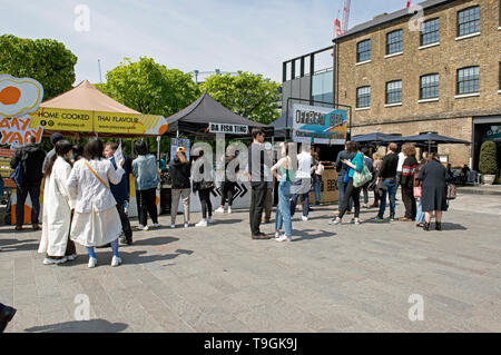 Bancarelle prodotti alimentari compresi Yaay Yaay e da pesce Ting con persone davanti il granaio di accodamento Square Kings Cross, London Borough of Camden Inghilterra Gran Bretagna REGNO UNITO Foto Stock