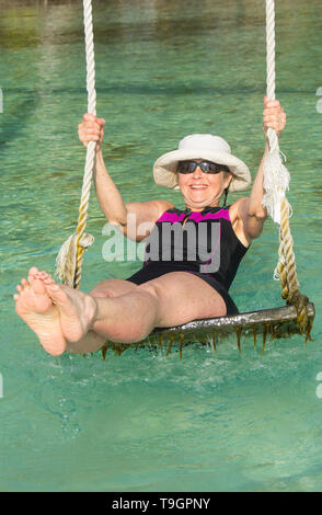 La donna gode di swing in acque tropicali e piattaforme Palapa, a nord lungo il Coco Plum Caye Belize Foto Stock