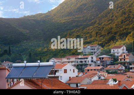 Moderne fonti di caloriferi di acqua solari sono installati sulla piastrella arancione del tetto della casa sullo sfondo di un paesaggio di montagna in Montenegro Foto Stock