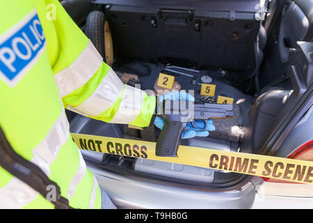 Funzionario di polizia in possesso di una pistola ha scoperto in un baule auto, confezioni di farmaci con evidenza i marcatori in background Foto Stock