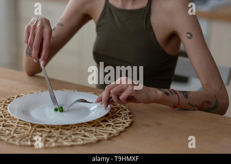 Donna che mantiene il coltello e forchetta mentre mangia solo tre piselli verdi Foto Stock