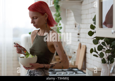 Skinny i capelli rossi donna con tatuaggi mangiare insalata di verdure Foto Stock