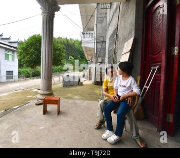 (190519) -- NANCHANG, 19 maggio 2019 (Xinhua) -- Lin Fusheng (L) Chat con sua figlia davanti alla loro casa in Lichuan County, Cina orientale della provincia di Jiangxi, 16 maggio 2019. Lin Fusheng, un abitante di un villaggio da Hualian villaggio di Huashan township di Lichuan County, subito da handicap fisico a causa della paralisi infantile. Nonostante che, Lin bloccato con il suo sogno di diventare un pittore. Come Lichuan County assistito a un rapido sviluppo dell industria della pittura a olio nel 2013, Lin è ritornato nella sua città natale e cresciuto come un pittore professionista con l aiuto del governo locale. Ora Lin possiede uno studio a un'oi Foto Stock