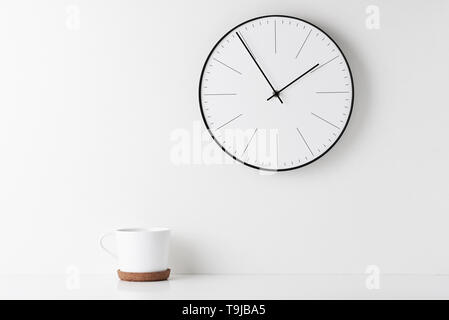 Vista frontale tavolo rotondo con orologio da parete e cup su sfondo bianco. Home office il minimo spazio di lavoro scrivania Foto Stock