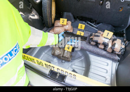 Funzionario di polizia in possesso di una pistola ha scoperto in un baule auto, confezioni di farmaci con evidenza i marcatori in background Foto Stock