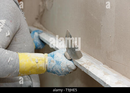 Il processo di livellamento di intonaco grezzo sulla parete utilizzando una scheda. Foto Stock