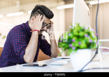 Stanco e preoccupato uomo indiano al lavoro in ufficio Foto Stock