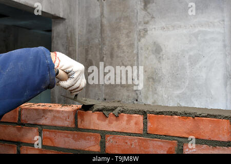 Mano nel processo di posa di un muro di mattoni rossi. Foto Stock