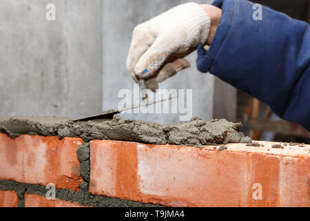 Mano nel processo di posa di un muro di mattoni rossi. Foto Stock