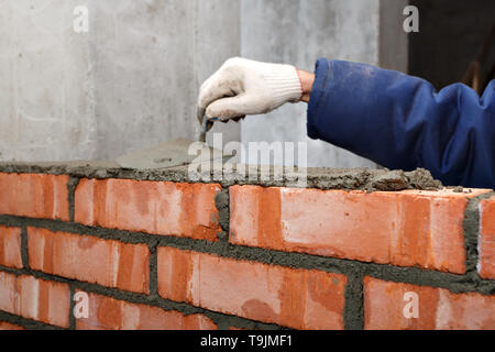 Mano nel processo di posa di un muro di mattoni rossi. Foto Stock