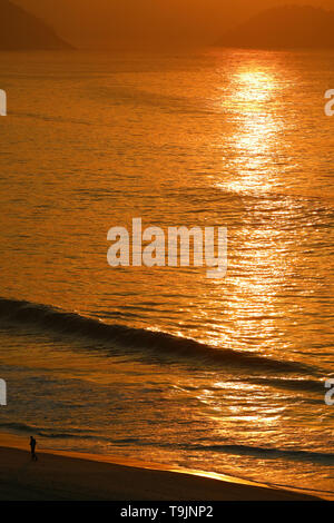Luce del sole di mattina riflettendo sull Oceano Atlantico con silhouette di un uomo a camminare sulla spiaggia di Copacabana, Rio de Janeiro, Brasile Foto Stock