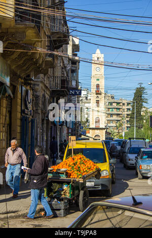 Tripoli, Libano - 15 Gennaio 2016: uomo vendere i tangerini nel centro cittadino e la Al-Tell Torre dell Orologio a Tripoli in Libano Foto Stock