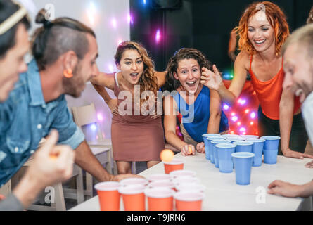 Gruppo di happy amici giocare Pong della birra nei pub cocktail bar - Giovani millennial persone divertirsi facendo festa di alcol giochi di notte Foto Stock