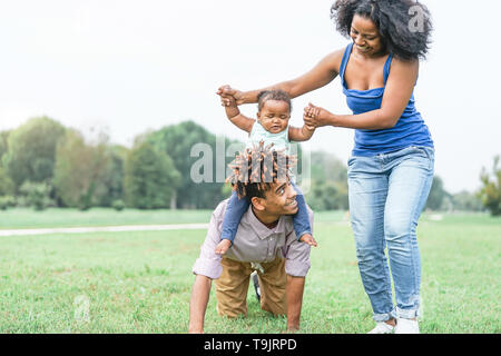 Felice famiglia africana divertirsi in un parco pubblico outdoor - il padre e la madre a giocare con la loro figlia durante un fine settimana giornata di sole Foto Stock