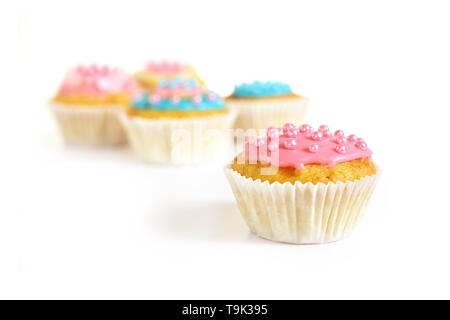 Muffin o cupcake con glassa rosa e perle di zucchero, più i tortini sfocata in background, isolato con ombre sul bianco, spazio copia, messa a fuoco selezionata Foto Stock