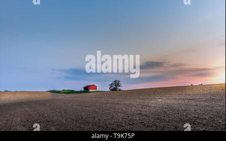 Idilliaco fattoria con granaio rosso nel Maryland campagna con campi arati al tramonto durante la primavera Foto Stock