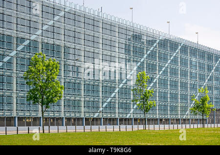 Leiden, Paesi Bassi, 18 Maggio 2019: prato e tre giovani alberi in fornt della facciata di vetro di un garage per il parcheggio presso il bio parco della scienza Foto Stock