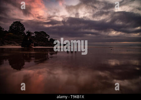 Spiaggia di riflessione del sorgere del sole in Devonport Tasmania, giovani uomini che chiacchierano tra loro Foto Stock