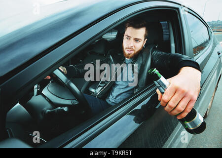 Un ubriaco alla guida di una vettura con una bottiglia di alcool in mano.Un uomo detiene una ruota motrice e una bottiglia di birra. Foto Stock