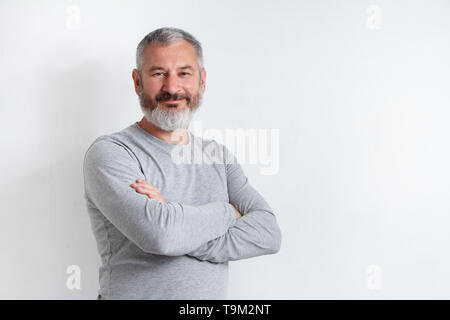 A mezza lunghezza Ritratto di un grave grey-haired uomo barbuto in grigio di una t-shirt su uno sfondo bianco. Foto Stock