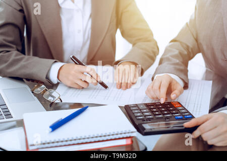 Due femmina commercialisti contando sulla calcolatrice entrate fiscali per formare il completamento mani di close-up. Business e concetto di audit. Foto Stock