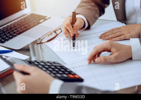 Due femmina commercialisti contando sulla calcolatrice entrate fiscali per formare il completamento mani di close-up. Business e concetto di audit. Foto Stock