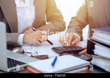 Due femmina commercialisti contando sulla calcolatrice entrate fiscali per formare il completamento mani di close-up. Business e concetto di audit. Foto Stock